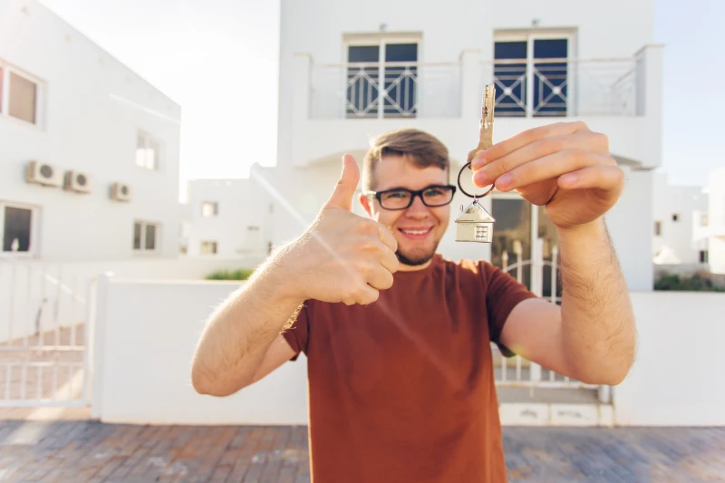 Man holding keys in front of home.